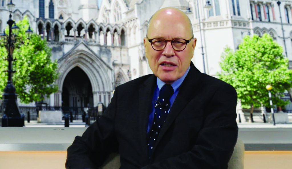 Man wearing glasses and a dark suit and tie in front of an image of the Royal Courts of Justice