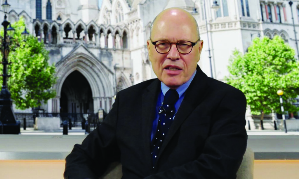 Man wearing glasses and a dark suit and tie in front of an image of the Royal Courts of Justice