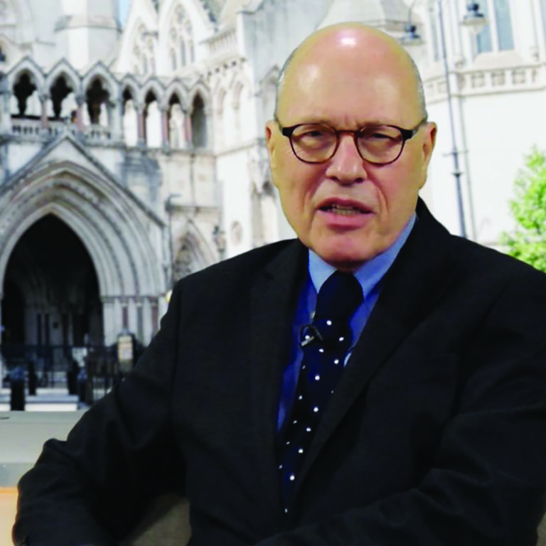 Man wearing glasses and a dark suit and tie in front of an image of the Royal Courts of Justice