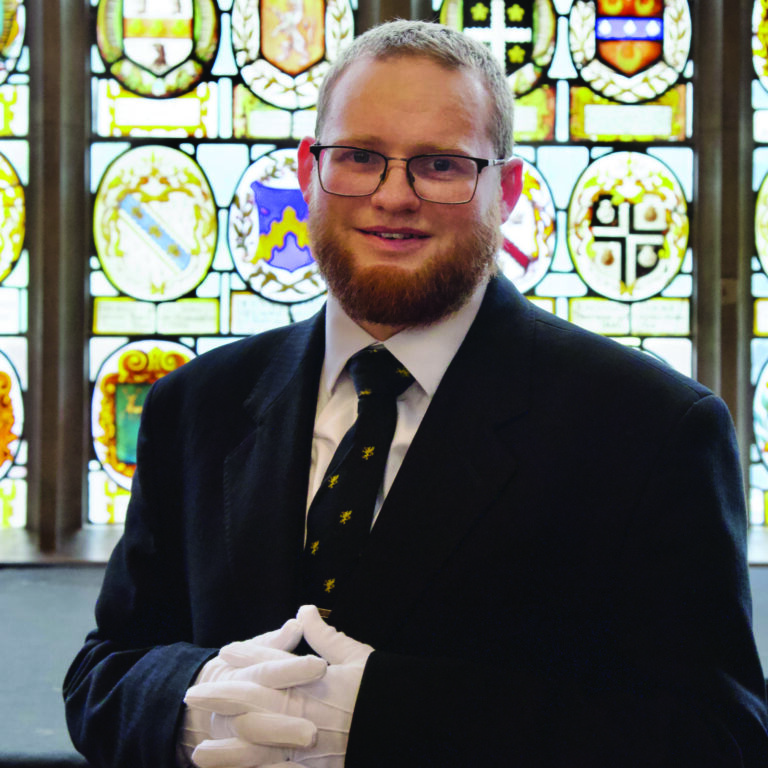 Philip Craig, Hall Butler, standing infront of stained glass windows in Hall