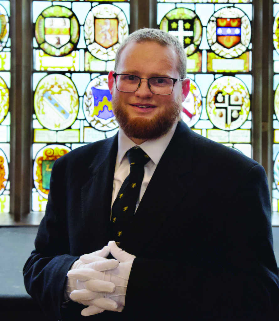 Philip Craig, Hall Butler, standing infront of stained glass windows in Hall
