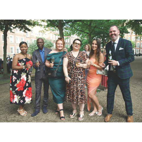 A group of six people standing in the Inn's gardens. They are smiling to camera, wearing suits and colourful party dresses and holding drinks.