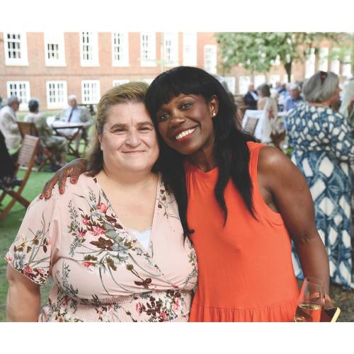 Two members smiling during a party in the gardens wearing a pink floral dress and an orange sleevless dress