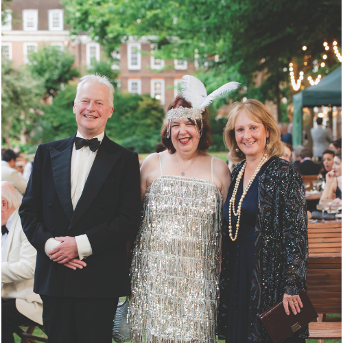 Three people smiling to camera. The man on the left wears a suit and bow-tie. The two women on the right wear 1920's themed sequin dresses.